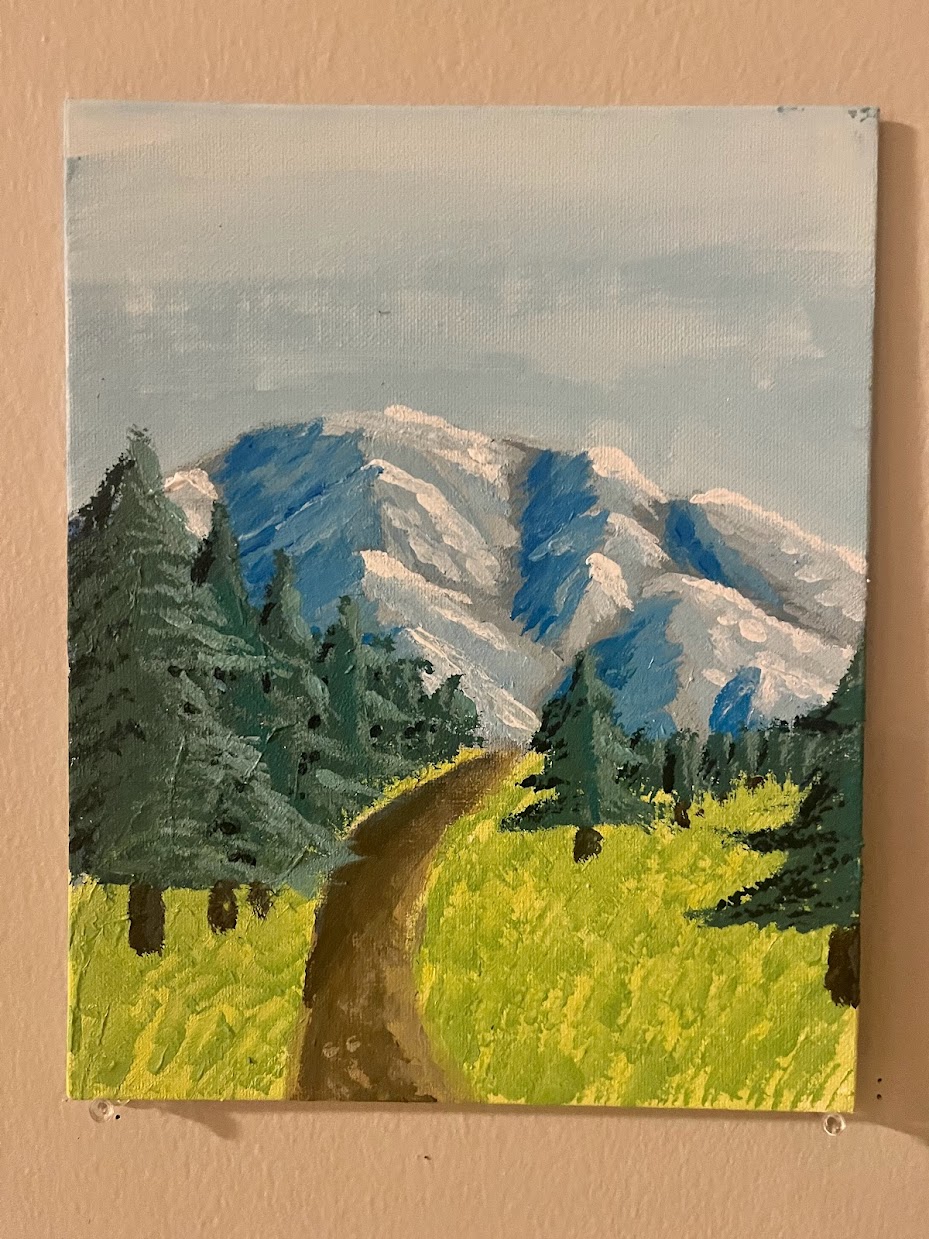 A dirt path winding through conifers towards a frozen blue mountain range under a misty pale blue sky.