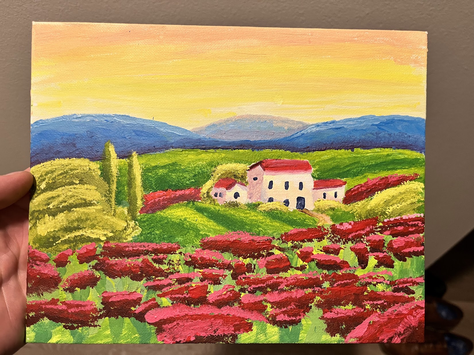 A tuscan manor in a vibrant green rose field, poking out of the rolling hills in the foreground, with the red setting sun beyond hazy deep blue mountains.